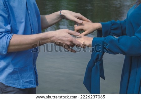 Close up partners holding hands concept photo. Romantic couple in blue clothes. Side view photography with lake on background. High quality picture for wallpaper, travel blog, magazine, article