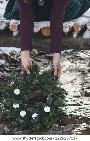 Close up Christmas wreath concept photo. Lady holding fir garland. Front view photography with forest brook on background. High quality picture for wallpaper, travel blog, magazine, article