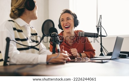 Female podcasters laughing and having a great time on an audio broadcast in a home studio. Two happy women recording an internet podcast for their social media channel.