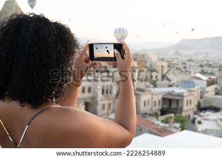 a tourist takes photos of hot air balloons in the mountains of Cappadocia on a mobile phone