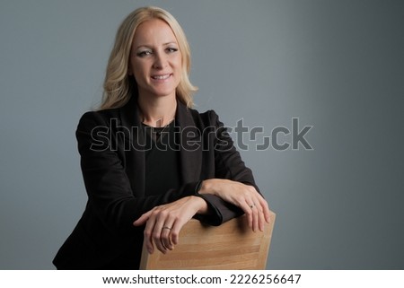 Portrait of a smiling business woman wearing black suit sitting on the chair with crossed arms isolated on gray background. Royalty-Free Stock Photo #2226256647