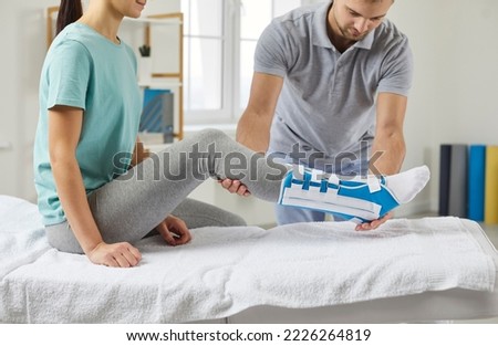 Woman with a splint on her shin lies on a couch in the physiotherapist's office in the rehabilitation center. Male physiotherapist examines a patient's leg during a rehabilitation consultation  Royalty-Free Stock Photo #2226264819