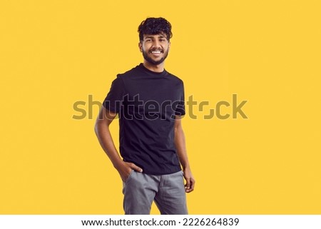 Young cheerful attractive South Asian man with dark curly hair posing with smile in casual clothes holding hand in pocket of trousers stands on solid yellow background in studio. Ethnic Indian human Royalty-Free Stock Photo #2226264839