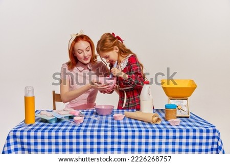 Portrait of mother and daughter cooking cake together isolated over grey background. Spending time together. Concept of beauty, retro style, fashion, elegance, 60s, 70s, family. Copy space for ad Royalty-Free Stock Photo #2226268757