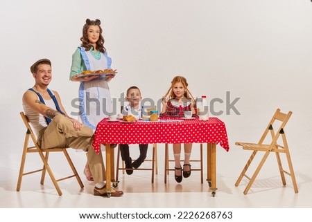 Portrait of beautiful young family sitting at the table and having breakfast together over grey background. Concept of beauty, retro style, fashion, relationship, 60s, 70s, family. Copy space for ad Royalty-Free Stock Photo #2226268763