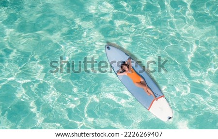 Asian woman in bikini sleep and relax on paddle board on the beach in summer time