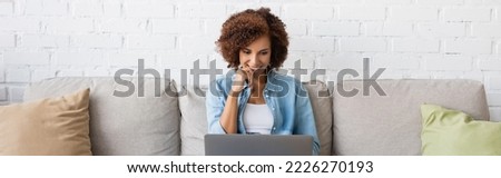 happy african american woman using laptop while sitting on couch and working from home, banner