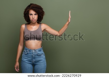 Serious african american woman showing stop gesture and looking at camera isolated on green