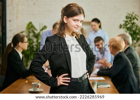 Young beautiful businesswoman got job promotion, done successful project, look at the camera, smiling in modern office during meeting with colleagues. Concept of business, finance, success and career