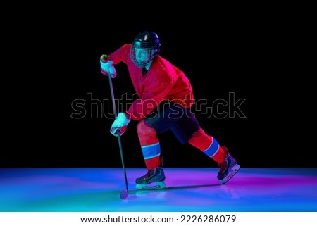 Training of male ice hockey player wearing hockey jersey, uniform and sports helmet in motion isolated over dark background in neon light. Concept of sport, action, movement, competition