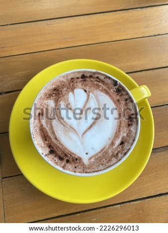 A yellow cup of Hot chocolate with leaves drawn on the top to booster the day