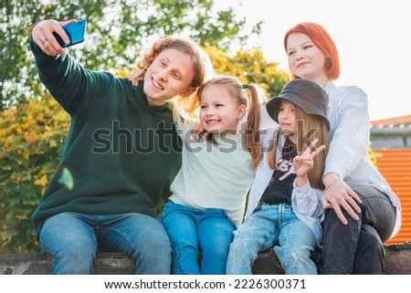 Portraits of three smiling sisters and brother teen taking selfie portrait using a modern smartphone camera. Careless happy young teenhood, childhood time and modern technology concept image.