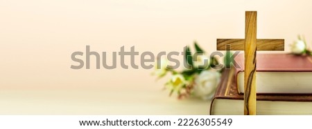 Religion banner with wooden cross with closed red Christian bibles with white flowers on a light gradient background with copy space. Easter holiday. Christian religion background. Front view