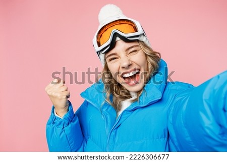 Close up winner snowboarder woman wear blue suit goggles mask hat ski jacket do selfie shot pov mobile cell phone isolated on plain pastel pink background Winter extreme sport hobby trip relax concept