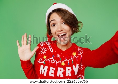 Close up merry young woman wear knitted xmas sweater Santa hat posing do selfie shot pov mobile cell phone waving hand isolated on plain pastel green background. Happy New Year 2023 holiday concept