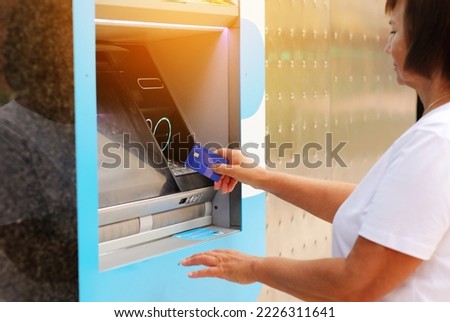 mature woman with card by ATM. Female with credit card withdrawing money from ATM using NFC contactless wifi system. Wireless authentication and data transmission security in finance and banking