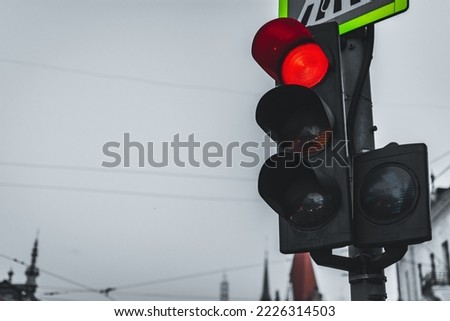 Black traffic semaphore with red light, under a pedestrian crossing sign, stopping traffic in an urban area