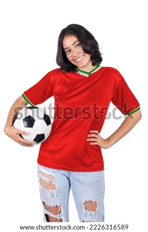 Portrait of young woman smiling with red jersey of her team from her favorite country IR IRAN holding a soccer ball on white background. Royalty-Free Stock Photo #2226316589