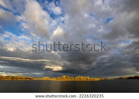 Dramatic and picturesque scene. Bright autumn landscape with thunderclouds over a pond. Artistic picture. The world of beauty and harmony.