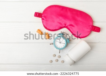 Sleeping mask, alarm clock, insomnia pills and ear plugs on a white wooden background. The concept of rest, sleep quality, good night, insomnia and relaxation. View from above. flat lay