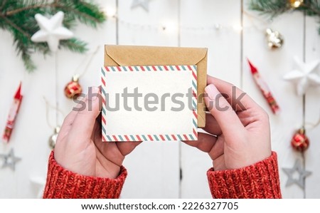 Envelope and blank Christmas card in female hands, top view.
