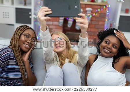 Girls take a selfie with a tablet next to a fireplace decorated for Christmas.