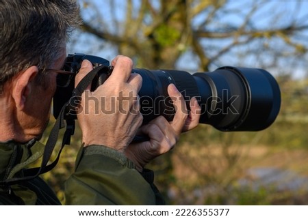 Man with telephoto lens captures a picture at the estuary. Middle aged gentleman   is bird watching and pans his camera as the bird fly's by. All Natural wildlife colours.