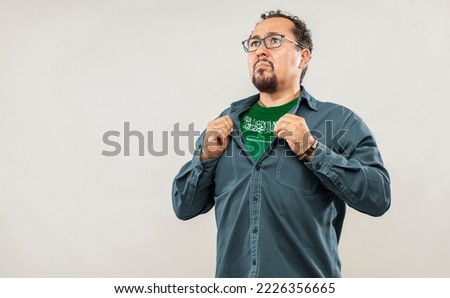 Fan man of 40s proud to show the jersey of the soccer team of his country Saudi Arabia under his shirt, on white background