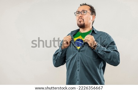 Fan man of 40s proud to show the jersey of the soccer team of his country Brazil under his shirt, on white background