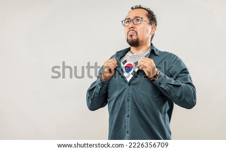 Fan man of 40s proud to show the jersey of the soccer team of his country Korea Republic under his shirt, on white background