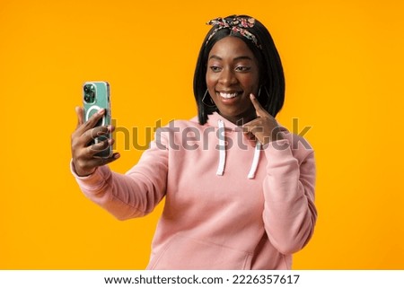 Happy african girl using her smartphone against yellow background.
