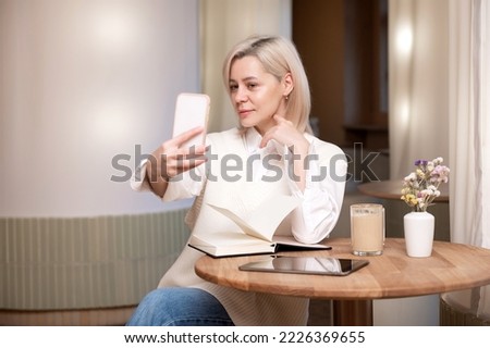 A cute girl takes a selfie and sits at a table in a cafe with a diary