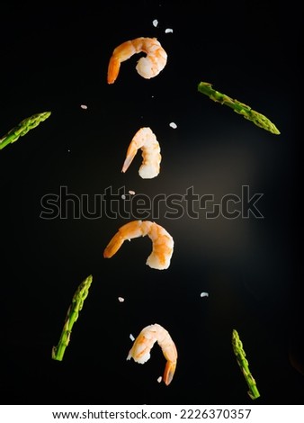 Culinary composition. On a black background, boiled shrimp, green asparagus shoots and grains of salt in a frozen flight. There are no people in the photo. Advertising, banner.