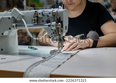 Seamstress or an employee of an Asian textile factory sewing on an industrial sewing machine. Close-up of the process of sewing fabric by a woman in production