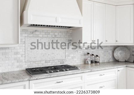A kitchen stovetop and hood with off white cabinets, a tiled backsplash, and marble countertop. Royalty-Free Stock Photo #2226373809