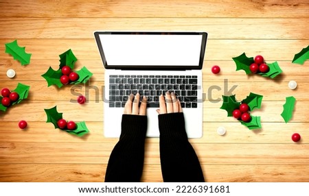 Person using a laptop computer with Christmas holly berries from above