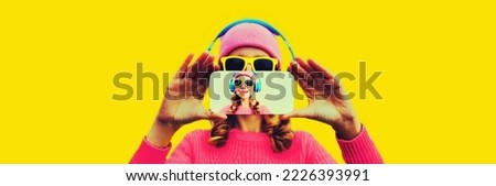 Close up of woman stretching her hands taking selfie picture with smartphone in headphones listening to music on yellow background