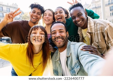 Happy young group of multiracial best friends having fun together outdoors. Millennial diverse people enjoying time together taking selfie portrait in city street
