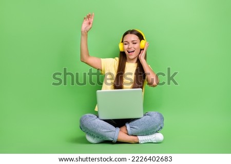 Photo of cheerful charming lady sit floor empty space use modern gadgets enjoy cool music isolated on green color background