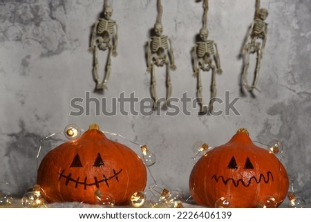 two orange pumpkins. two Jack lamp heads. garlands and skeletons in the background