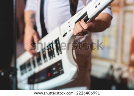 Concert view of a keytar synthesizer player with vocalist and musical jazz rock band orchestra performing in a background, electronic keyboard instrument guitar performer on a stage 