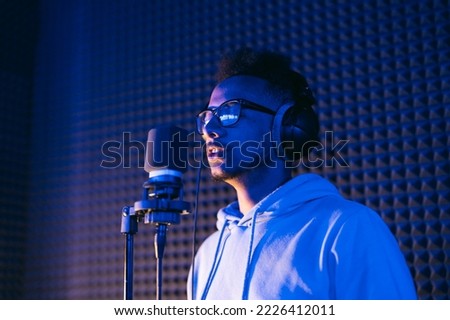 Male vocal artist, singer, podcaster with curly hair, headphones in sound studio recording new melody or album.