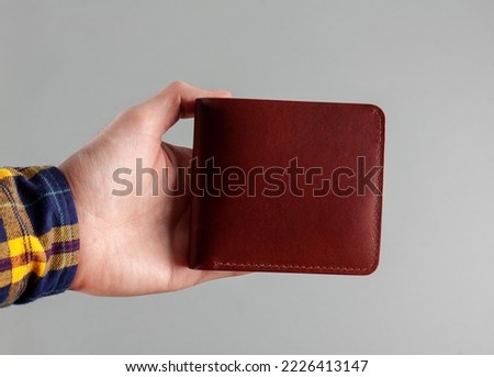 Leather wallet in hand on a gray background. For your logo.