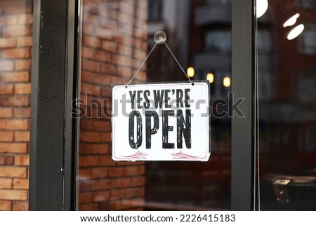 Inscription Yes we're open metal plate with black and white sign on glass door store, cafe, beautystore, barbershop after coronavirus lockdown quarantine. business reopen again. Royalty-Free Stock Photo #2226415183