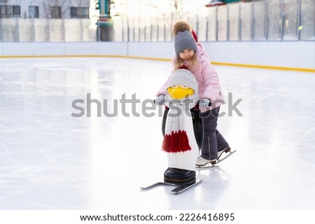A little girl is skating on an ice rink, holding on to a support, a child is learning to skate, winter entertainment for children. Royalty-Free Stock Photo #2226416895