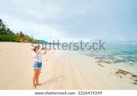 Vacation and technology. Young woman taking photo of beautiful tropical beach on smartphone.