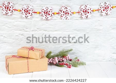 Christmas tree branch and gift boxes in craft paper with red bow on white brick wall background with snowflakes garland. New Year background with copy space, wallpaper, greeting card