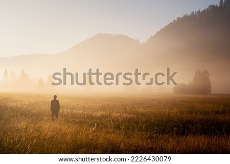 Man standing in a misty field looking to the future. Autumn morning and sunshine on a misty field. Royalty-Free Stock Photo #2226430079