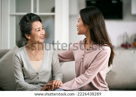 asian adult daughter sitting on couch at home chatting conversing with senior mother happy and smiling Royalty-Free Stock Photo #2226438289