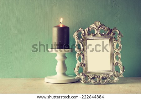 low key image of vintage antique classical frame and Burning candle on wooden table